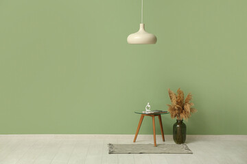Hanging lamp, pampas grass and coffee table with human figure and magazine near green wall in room