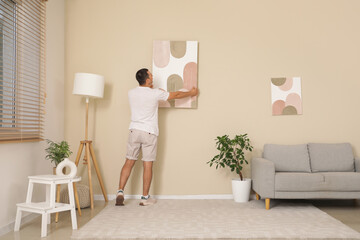 Young man hanging painting on beige wall at home, back view