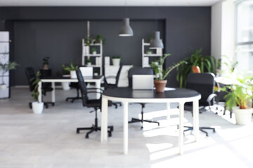 Blurred view of modern office with desks, shelf units and green plants