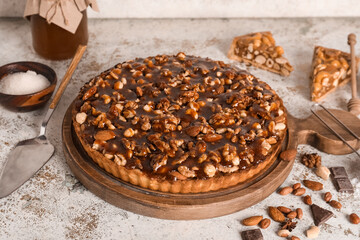Wooden board of sweet tart with different nuts and ingredients on white background