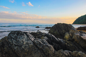 A large, weathered rock is positioned on a sandy beach adjacent to the ocean