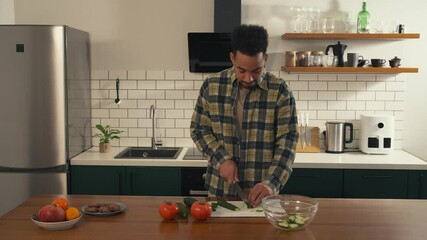 Calm morning scene of an African-American man slicing cucumber in the kitchen while preparing a fresh salad. The atmosphere feels peaceful and focused.