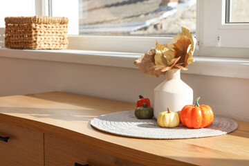 Vase with autumn leaves and pumpkins on commode in hallway, closeup