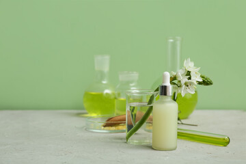 Laboratory glassware with ingredients and samples for preparing natural cosmetics on grey table near green wall