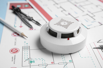 Modern smoke detector with supplies on evacuation plans, closeup
