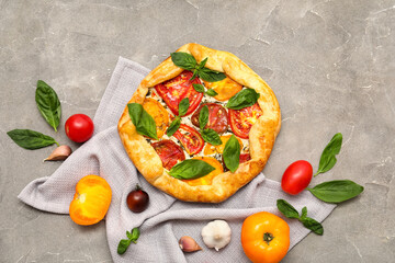 Composition with tasty tomato galette and fresh basil leaves on grunge background
