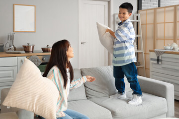 Young mother and her little son fighting pillows at home