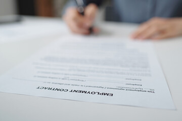 Closeup of unrecognizable person signing document in office with focus on Employment contract title...