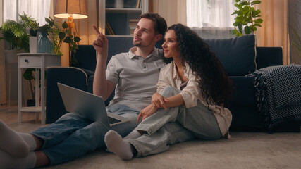 Obraz premium Multiracial couple shopping together happy talk pointing choose furniture ecommerce buy goods laptop at home boyfriend husband male Caucasian man guy talking girlfriend wife Hispanic woman girl female