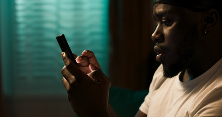 Relaxed man rests on the sofa with his phone, texting friends, exploring social media apps, and enjoying casual mobile games at home.