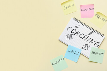 Notebook with word COACHING and sticky notes on beige background