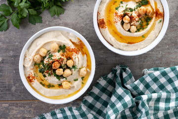 Chickpea hummus with olive oil, parsley and paprika in bowl on wooden table