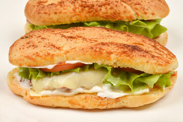 Two sandwiches made with garlic and oregano rolls, filled with mayo, cheese, lettuce, and tomato, are arranged on a white plate
