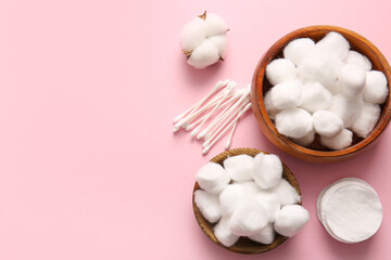 Wooden bowls with cotton balls, swabs, pads and flower on pink background