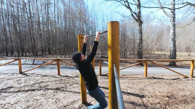 In a serene and peaceful park, an individual fervently engages in performing pullups, showcasing his unwavering commitment to strength training amid the tall trees and bright sky up above