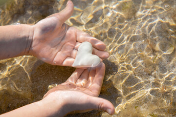 White heart in children's hands under water on a sandy beach. sun glare. Hello, summer, sun, vacation, travel, love for the sea, surprise, play with water
