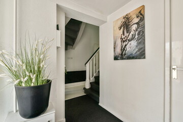 A contemporary entrance featuring a stylish staircase, a striking wall art piece, and a decorative plant, creating an inviting atmosphere for visitors.