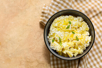 Bowl of tasty potato salad with green onion on beige grunge background