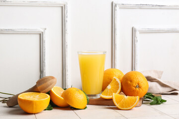 Glass of tasty juice with oranges, mint leaves and wooden juicer on white tile table