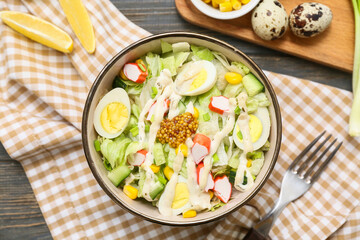 Bowl of salad with crab sticks, iceberg leaves, corn, quail eggs and cucumber on wooden background