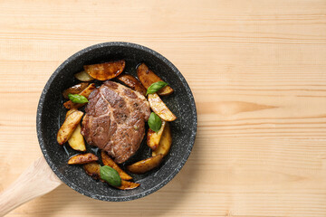 Frying pan with roasted steak and potato on wooden background