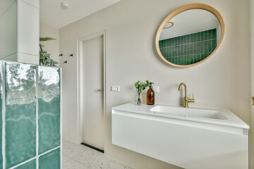 A stylish bathroom featuring green tiles, a circular mirror, and a white wall-mounted sink, creating a sleek and contemporary ambiance.