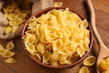 Bowl with raw pasta shells on wooden background, closeup