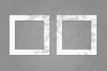 Natural light casts shadows from the wildflowers on 2 square frames of white textured paper lying on a gray facture background. Mock up with an overlay of plant shadows
