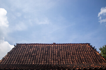 Traditional clay roof of a house against a backdrop of blue sky and clouds.