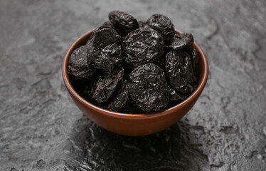 Bowl with dried prunes on black background