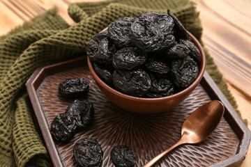 Bowl and tray with dried prunes on wooden background, closeup