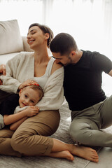 Fototapeta premium Happy family enjoying time together at home, kissing and cuddling on the floor