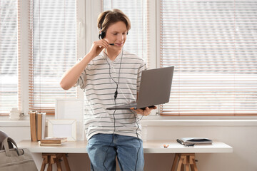 Teenage boy with laptop and headset working online at home