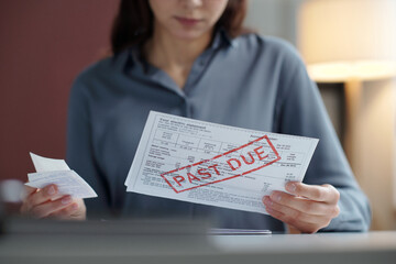 Close up of woman holding bills with past due notice while reviewing financial documents copy space