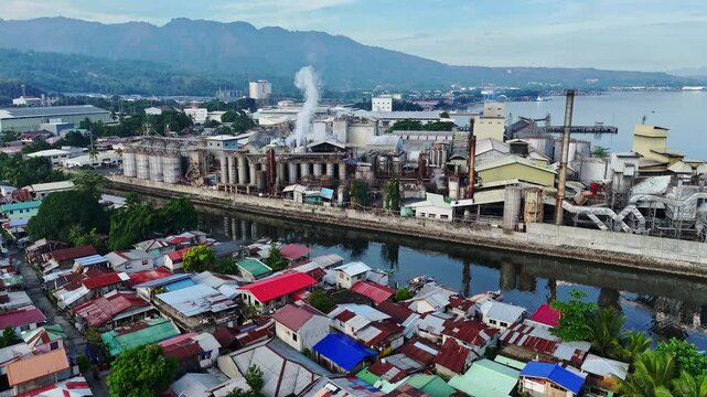 Sunrise illuminates coastal factories emitting smoke above shanty settlements in Cagayan de Oro, Philippines, highlighting environmental degradation and urban hardship.