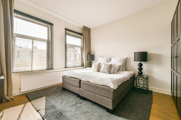 A spacious bedroom featuring large windows, soft lighting, and a neutral color palette. The stylish decor enhances the calming atmosphere.
