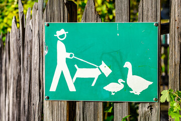 Sign indicating dog walking etiquette near ducks in a park setting on a sunny day surrounded by...