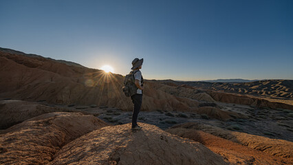 A man stands on an earthen rampart at sunset, when the golden hour comes. A traveler with a backpack and a hat overlooking the hills. Martian landscape.