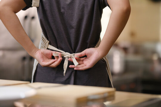 Close up of a young chef tying apron before preparing a meal in a commercial kitchen setting.