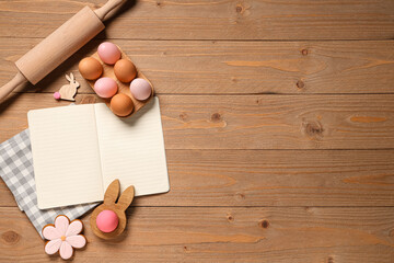 Composition with blank recipe book, beautiful Easter eggs and rolling pin on wooden background