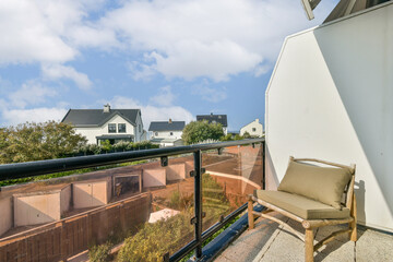 A beautifully designed modern balcony offers a comfortable chair and stunning views of a lush landscape and distant homes under a bright blue sky.