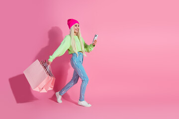 Young stylish woman wearing colorful casual clothes posing with shopping bags against a pink...