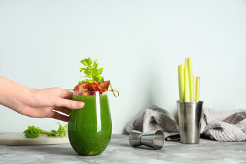 Female hand holding glass of green bloody mary cocktail with bacon and celery on colorful background