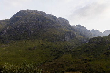 Golden sunset over calm lakes and clear water reflections in The Trossachs and Loch Lomond. Long winding roads cross green hills and mountains in a peaceful, awe-inspiring natural landscape. Exploring