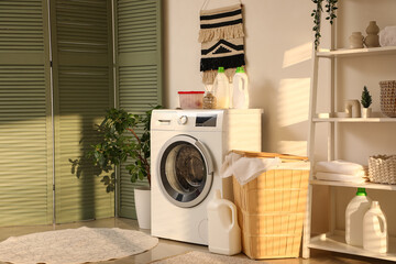 Stylish laundry room with modern washing machine, houseplant and bottles of detergent