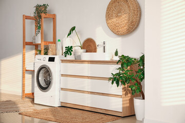 Stylish laundry room with modern washing machine, dresser, sink and bottles of detergent