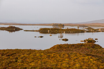 Golden sunset over calm lakes and clear water reflections in The Trossachs and Loch Lomond. Long winding roads cross green hills and mountains in a peaceful, awe-inspiring natural landscape. Exploring