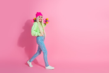 Young woman in colorful fashionable outfit with skateboard on pink background embodying trendy, stylish vibes