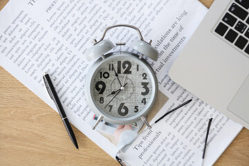 Alarm clock with newspaper, pen and laptop on table in office, top view