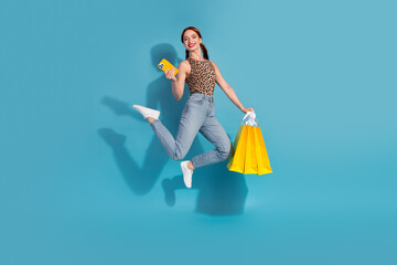 Young woman with bright shopping bags smiling and using a smartphone against a blue background, conveying happiness and style